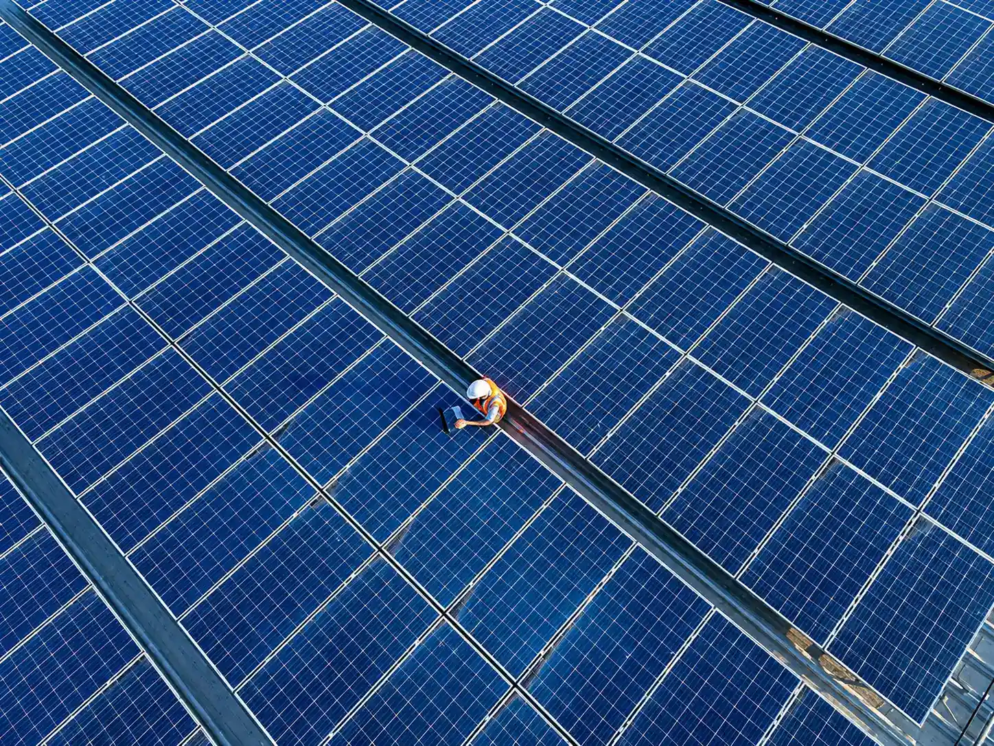 Aerial view of a technician in a hard hat inspecting a vast rooftop solar array