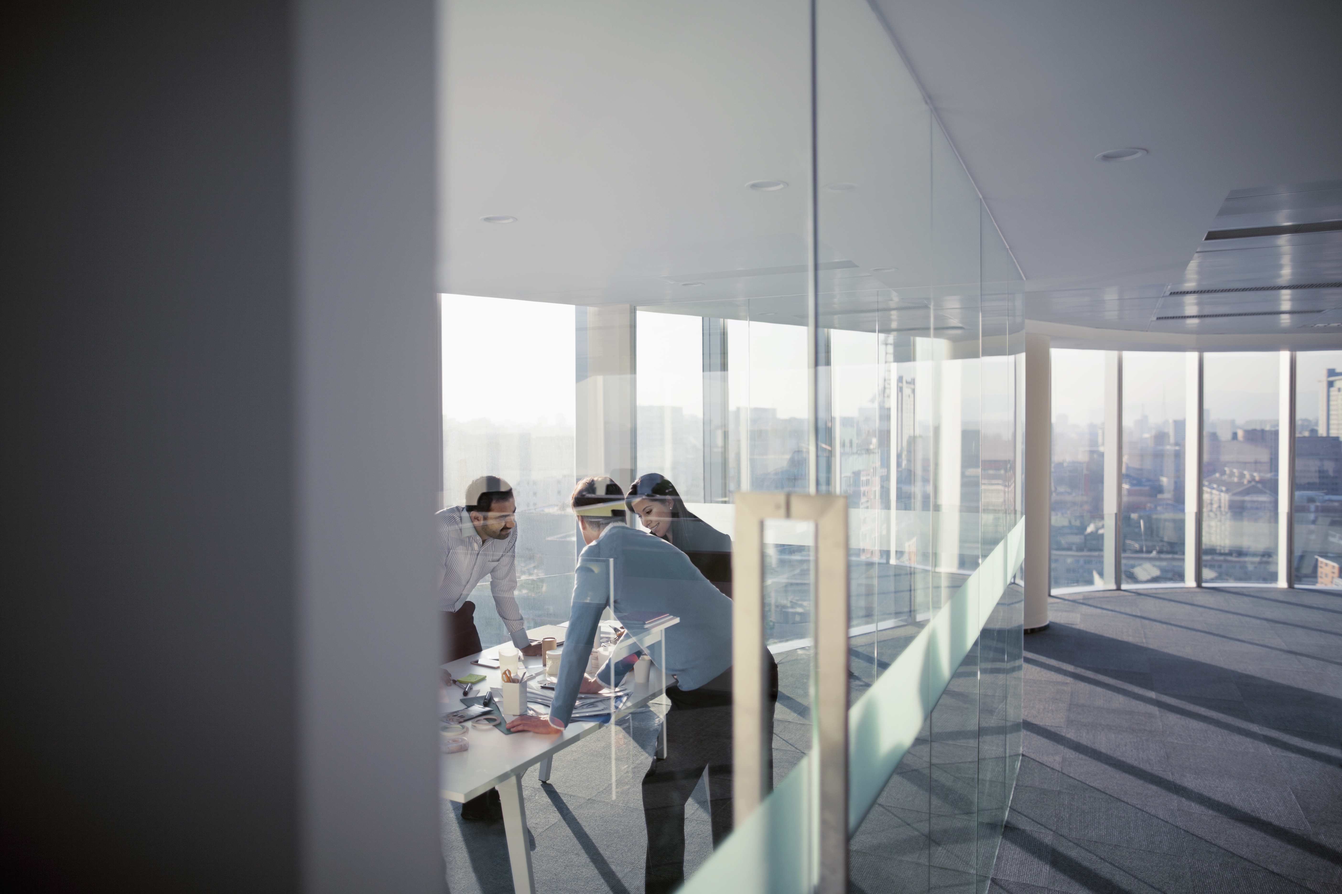 Three colleagues reviewing documents around a table in a high-rise meeting room
