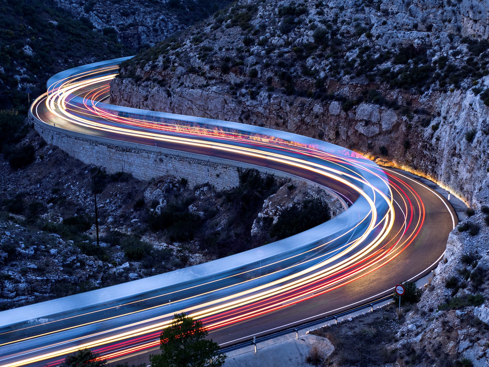 Long-exposure light trails on a winding mountain road at dusk