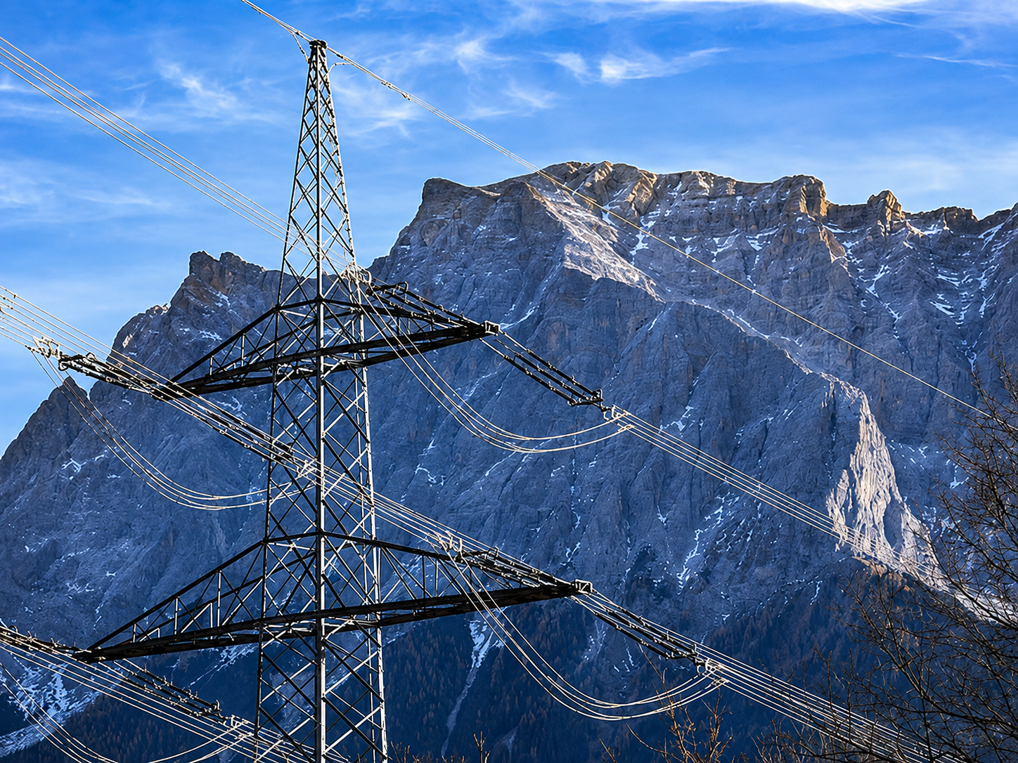 High-voltage transmission pylon and power lines against a mountain range — grid interconnection infrastructure